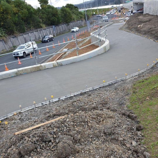 Curved concrete driveway under construction on a large site with cones and a work ute