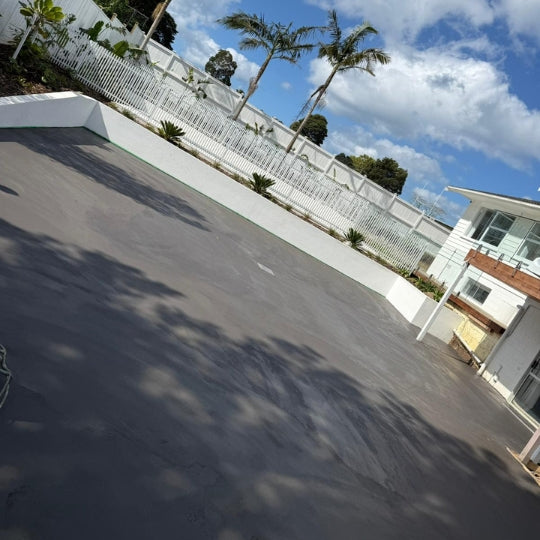 Smooth charcoal concrete driveway curving past a landscaped Auckland property