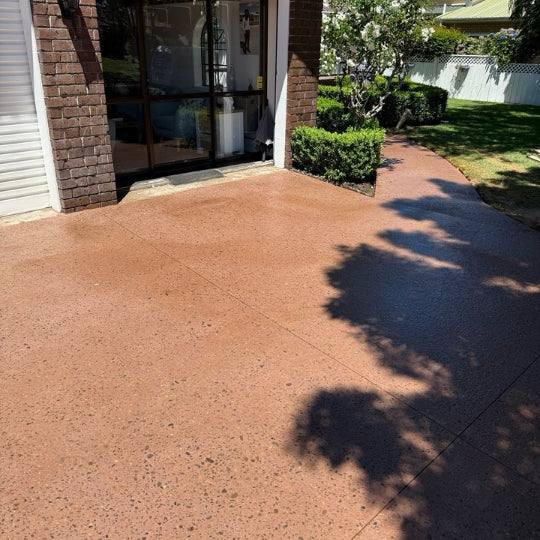 Coloured exposed-aggregate concrete patio beside a brick home and garden