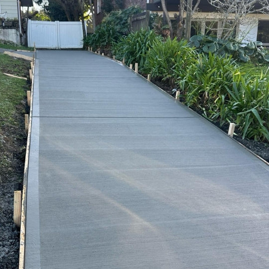 Smooth concrete path running between a white fence and a planted garden border
