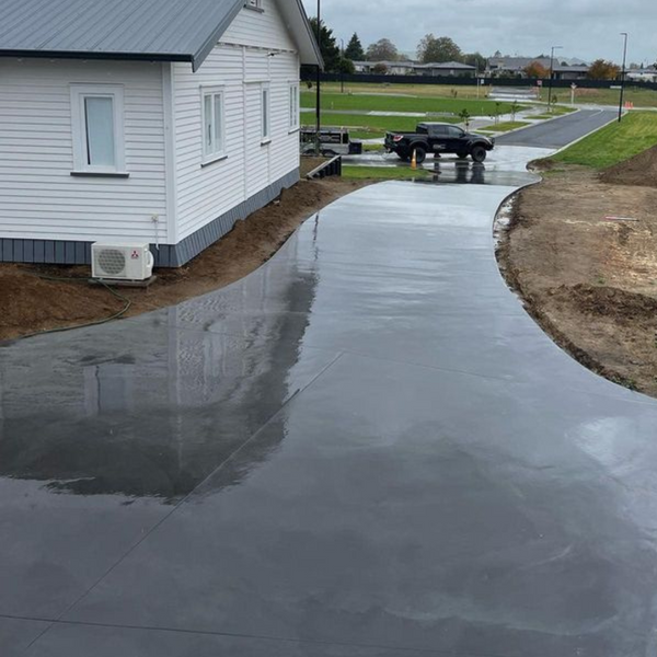 Curved plain concrete driveway beside a white house with open lawn