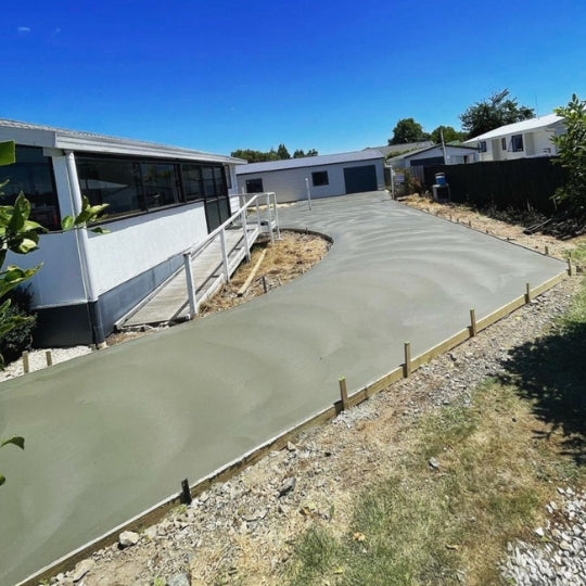 Wide curving concrete driveway in front of a modern white Auckland home
