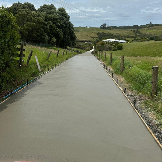 Long concrete driveway running through a rural Auckland property toward farmland