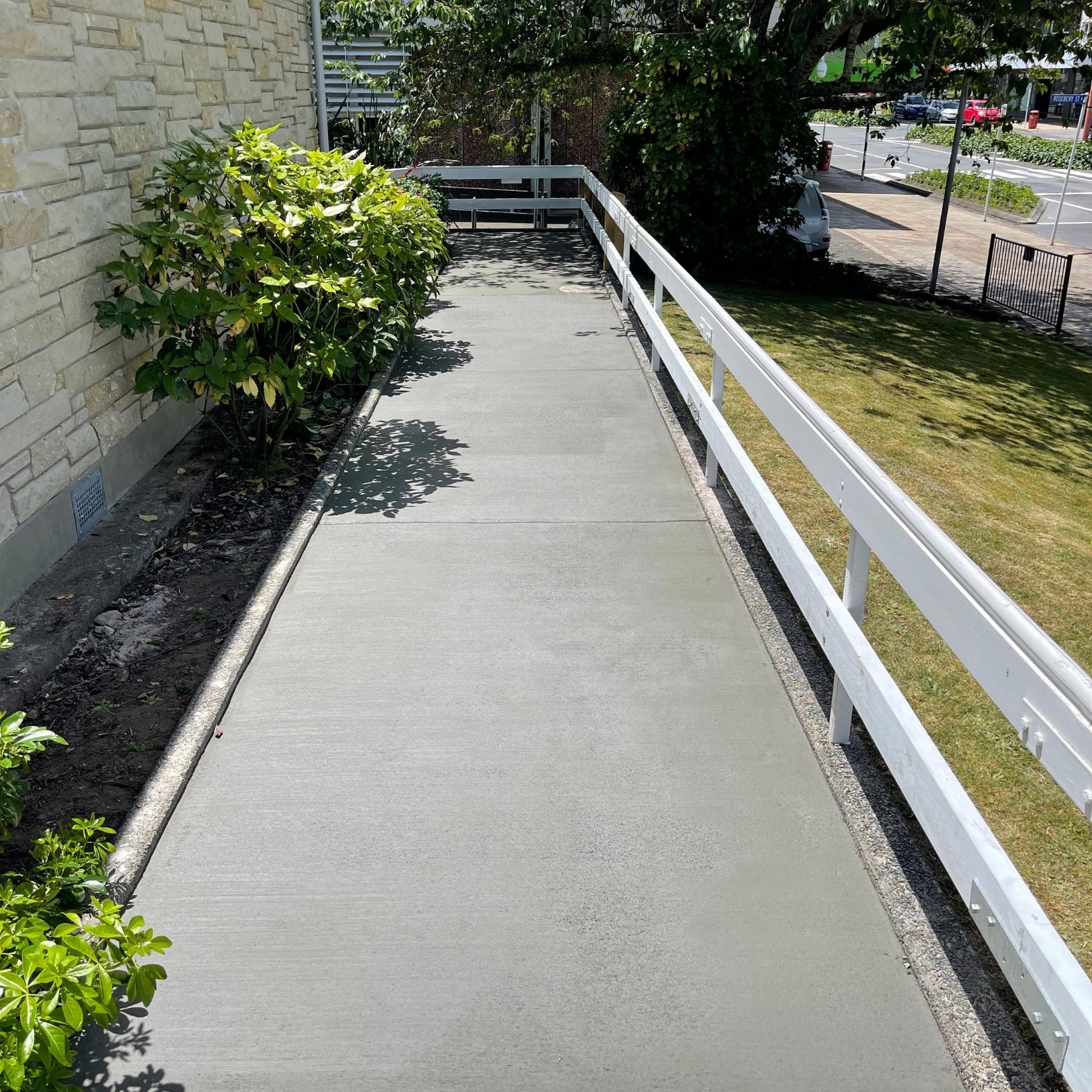 Curved concrete footpath beside a white post-and-rail fence and garden