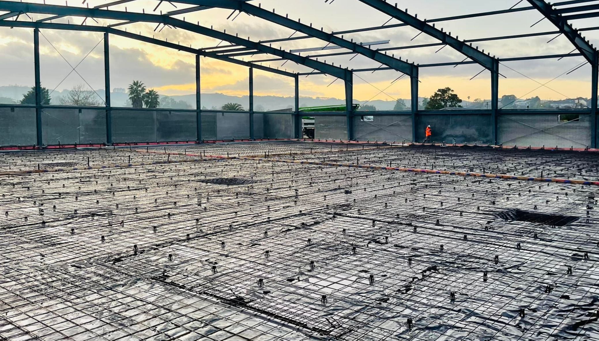 Steel-framed building under construction on a concrete floor at sunset