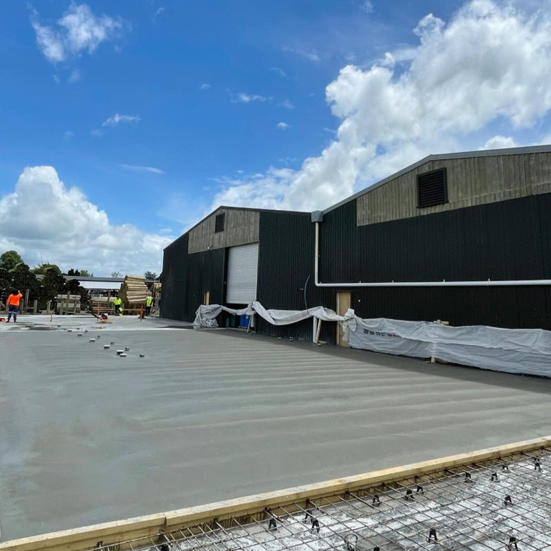 Freshly poured commercial concrete slab with reinforcing beside a green shed