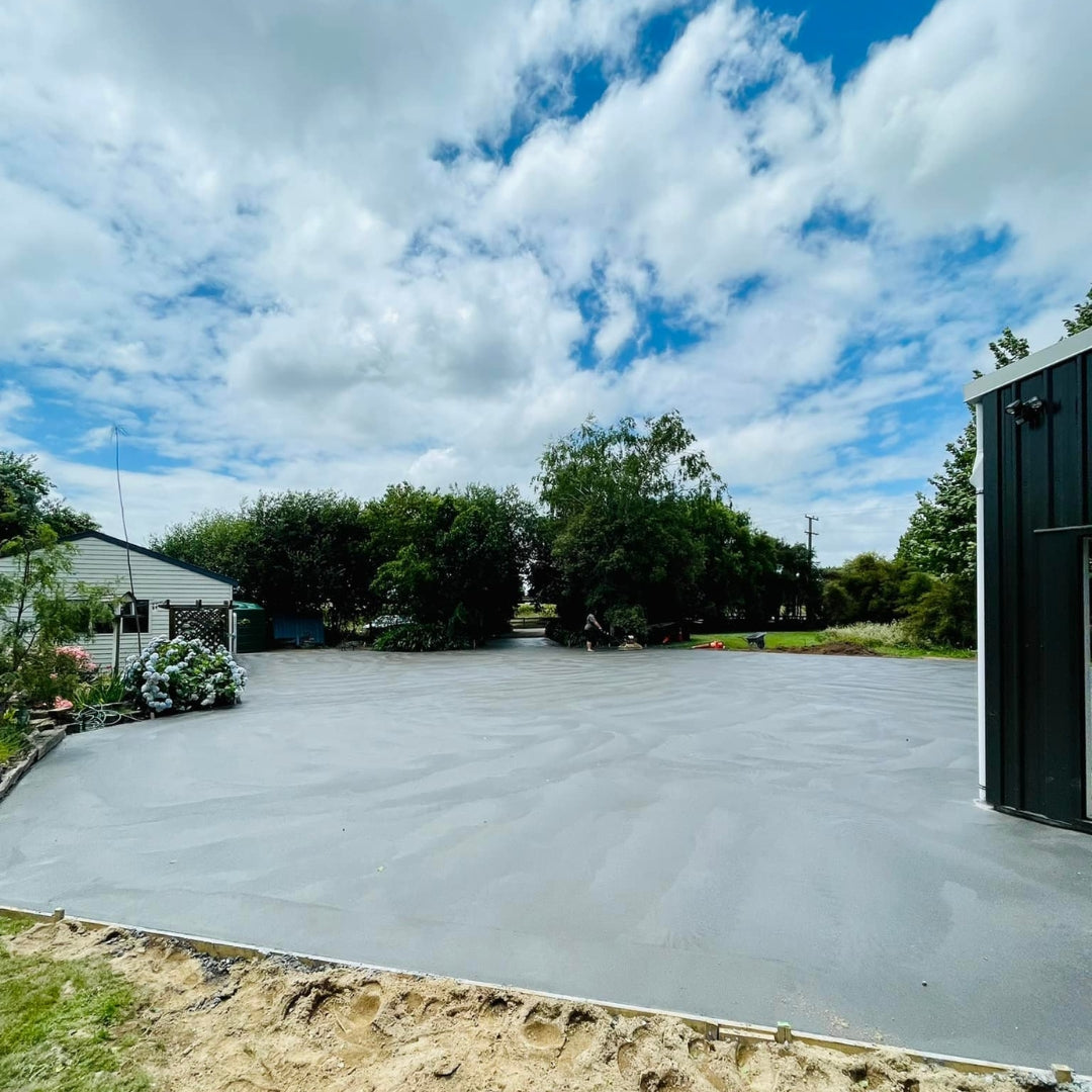 Large freshly poured concrete slab in a yard beside a green shed