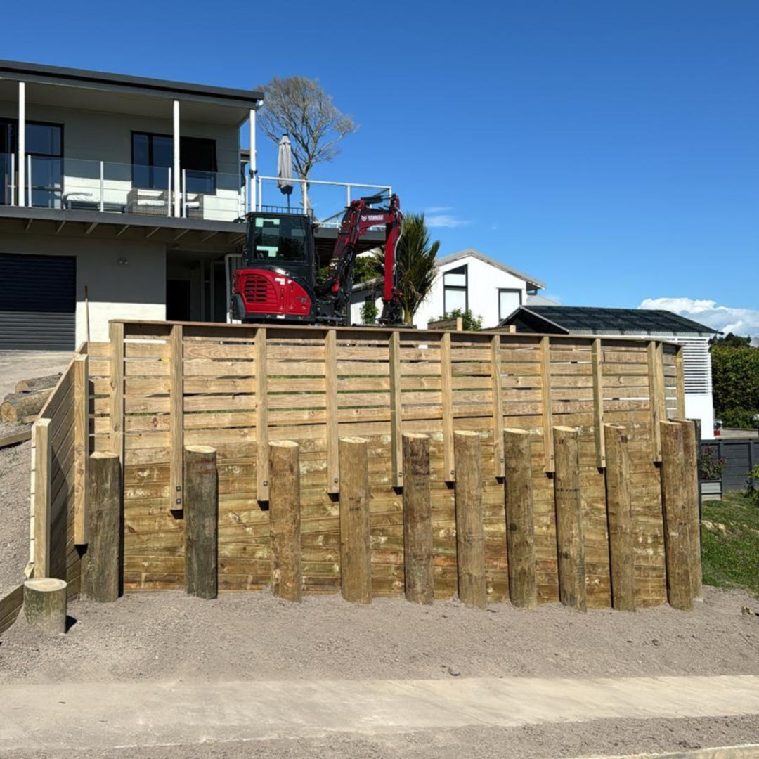 Timber pole retaining wall under construction with an excavator above