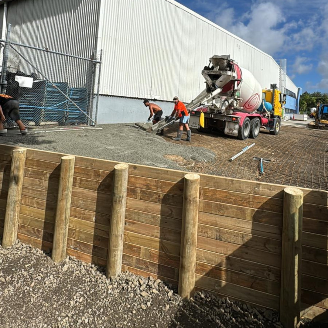 Timber pole retaining wall being built with a concrete truck pouring behind