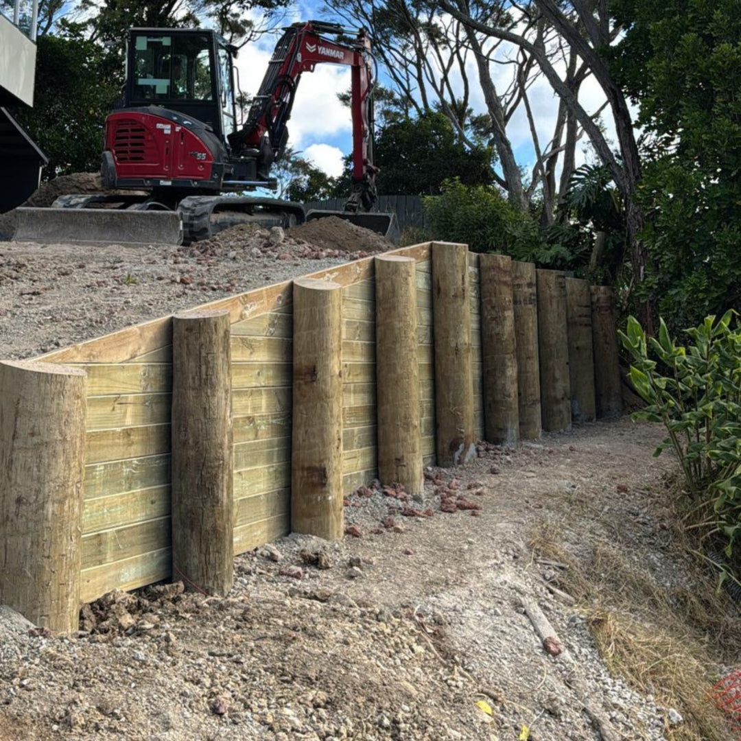 Timber pole retaining wall under construction with an excavator on the slope