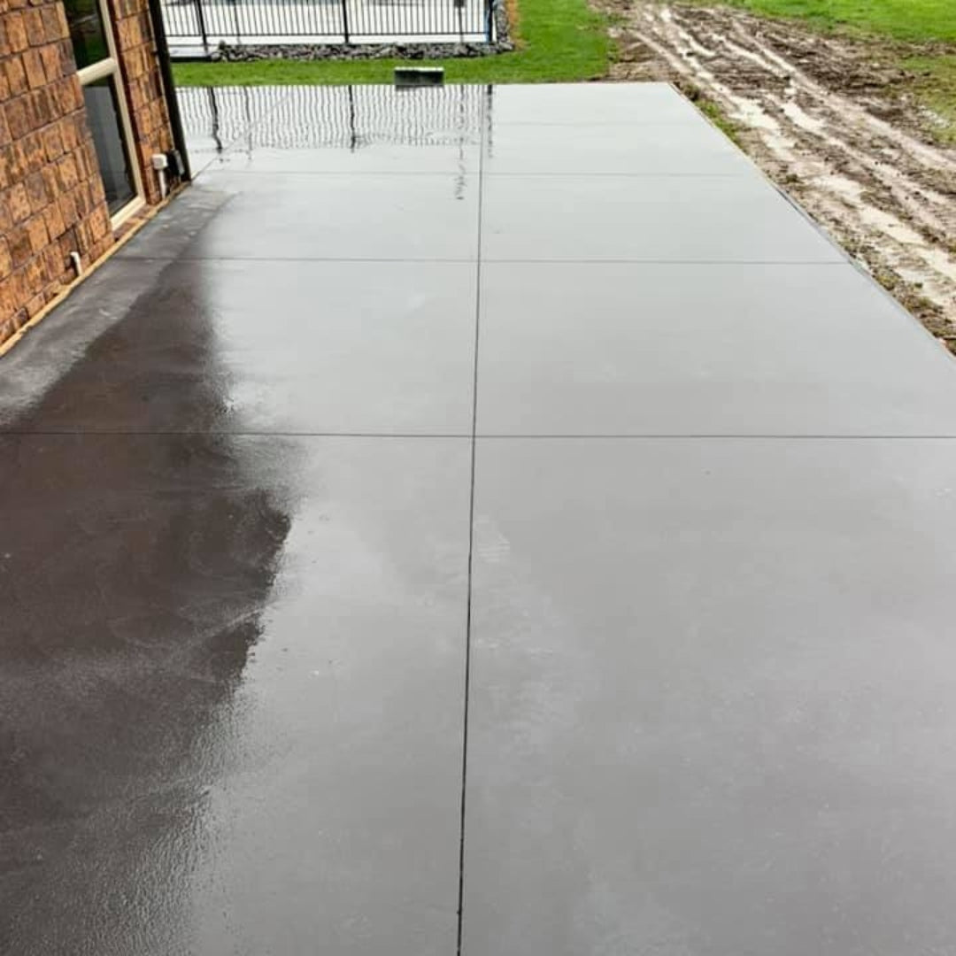 Freshly poured concrete driveway beside a brick home with timber formwork