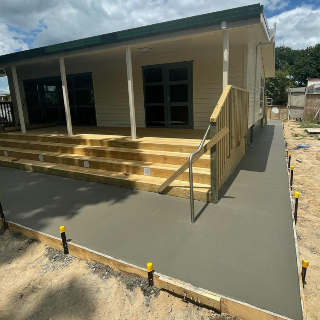 Fresh concrete poured around a piled weatherboard house during construction