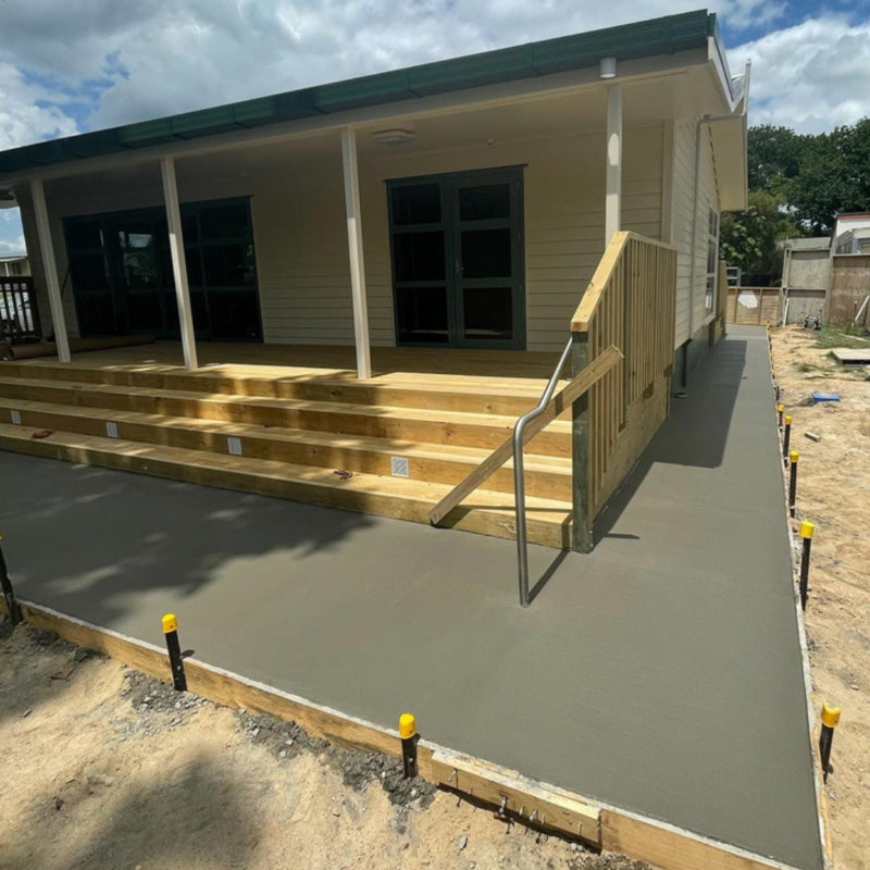 Fresh concrete poured around a piled weatherboard house during construction